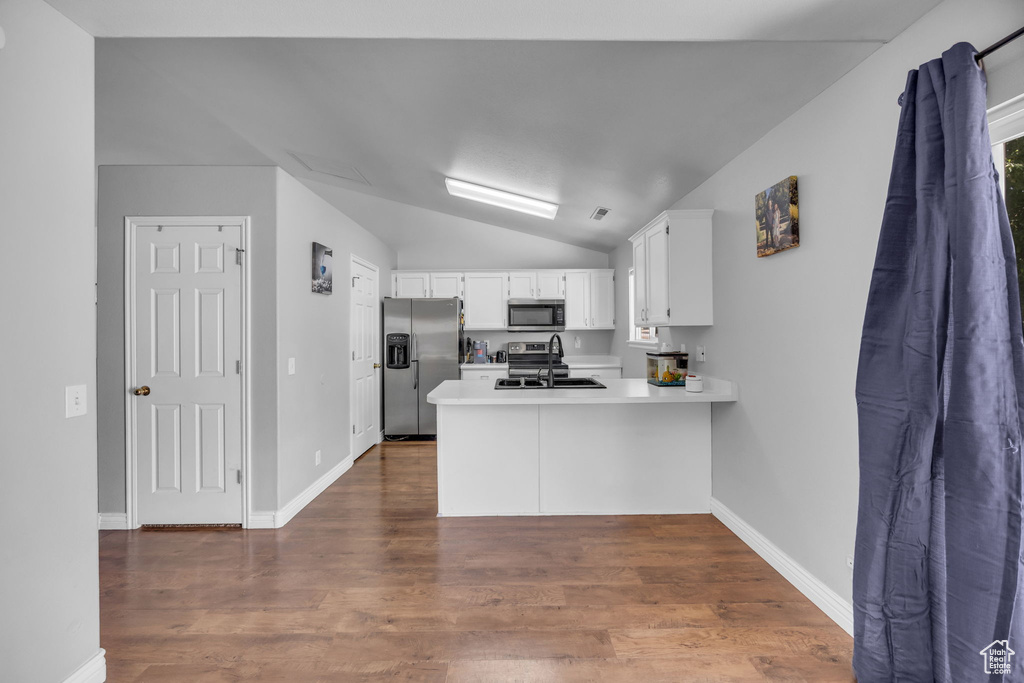 Kitchen featuring appliances with stainless steel finishes, a peninsula, lofted ceiling, a sink, and white cabinetry