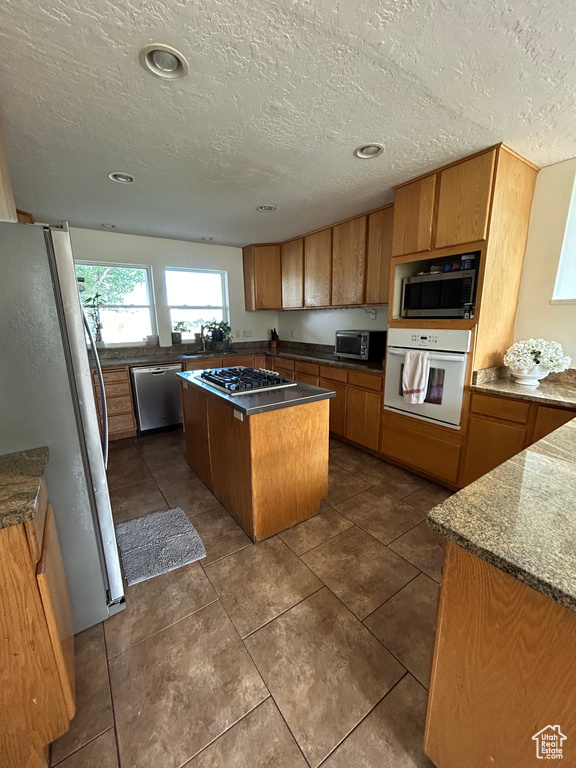 Kitchen with appliances with stainless steel finishes, a kitchen island, a textured ceiling, brown cabinets, and dark tile patterned flooring