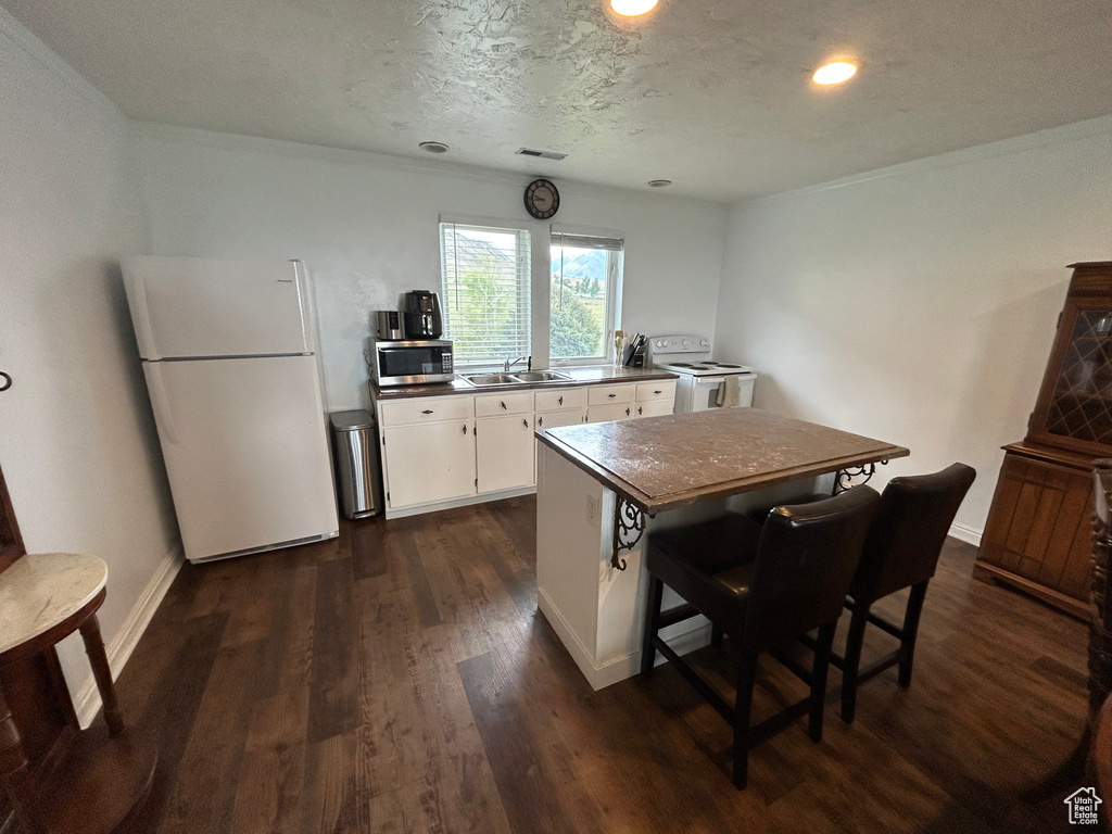 Kitchen featuring white appliances, a sink, dark wood-style flooring, white cabinetry, and a center island