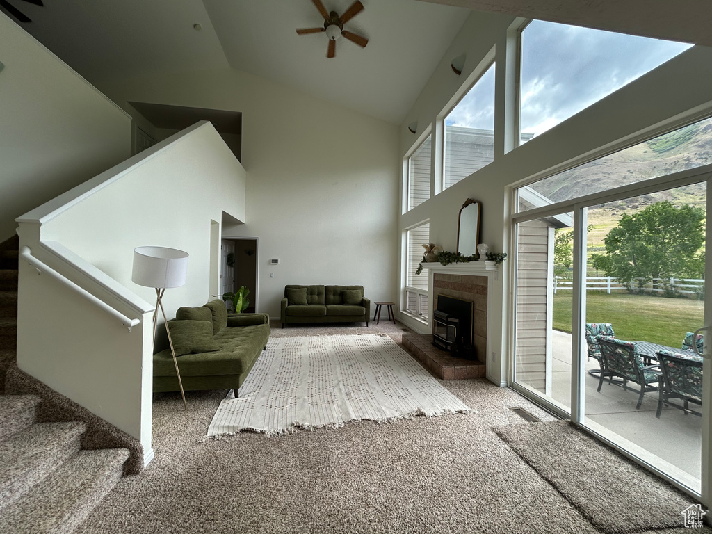 Living room with ceiling fan, high vaulted ceiling, carpet, stairway, and a fireplace