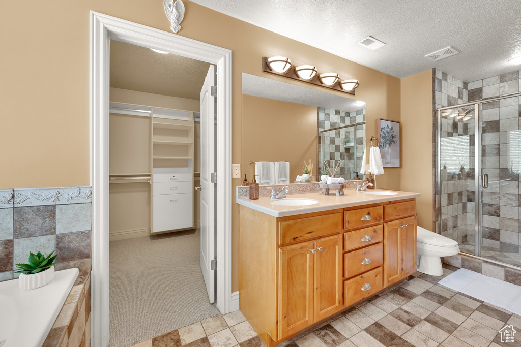 Full bath featuring a stall shower, double vanity, a textured ceiling, a walk in closet, and tiled bath