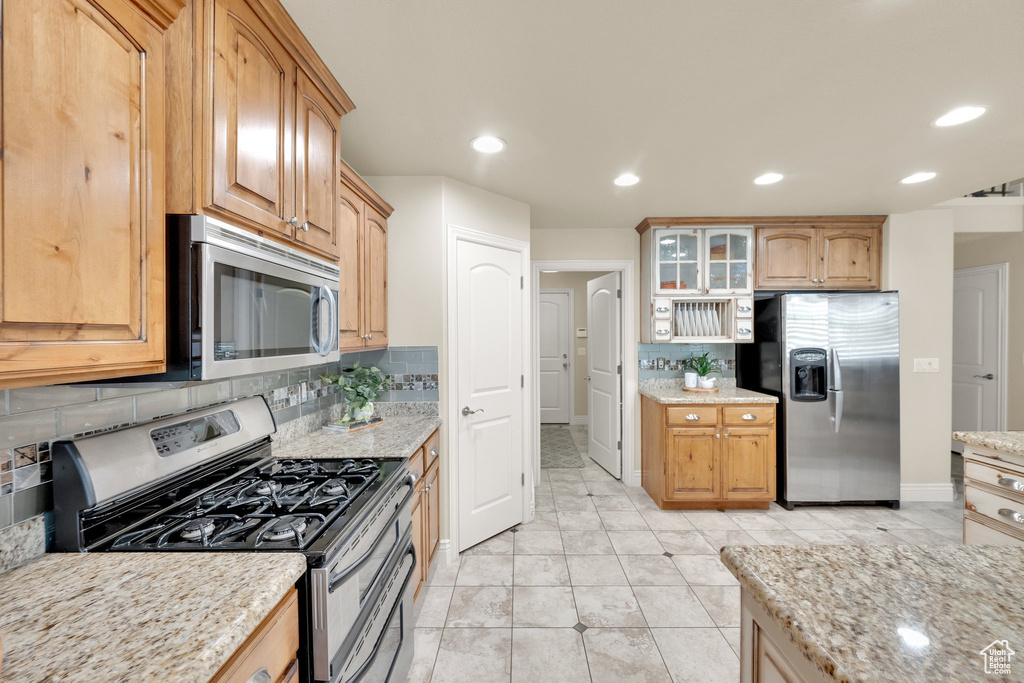 Kitchen featuring appliances with stainless steel finishes, backsplash, baseboards, light stone countertops, and recessed lighting