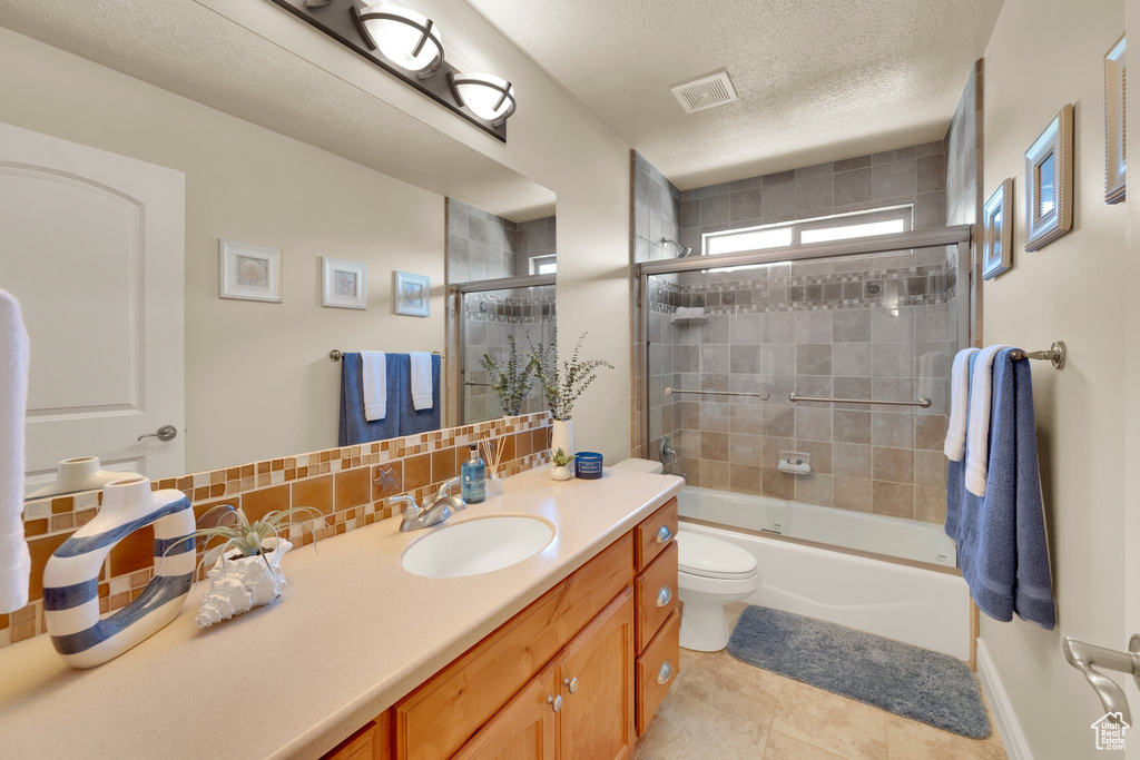 Full bathroom with vanity, toilet, bath / shower combo with glass door, tile patterned flooring, and tasteful backsplash