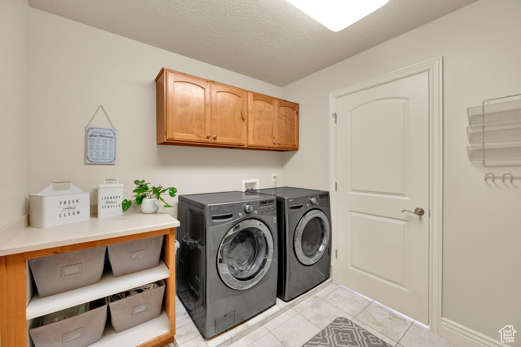 Laundry room with cabinet space, washing machine and clothes dryer, light tile patterned floors, and a textured ceiling