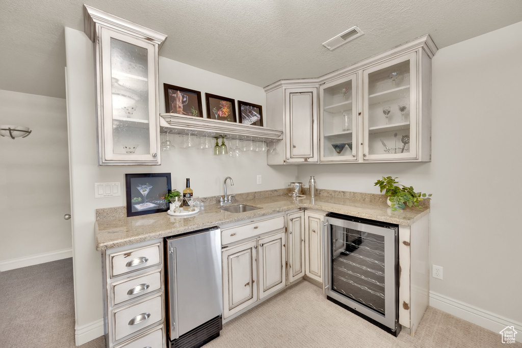 Indoor wet bar featuring beverage cooler, fridge, light colored carpet, a textured ceiling, and baseboards