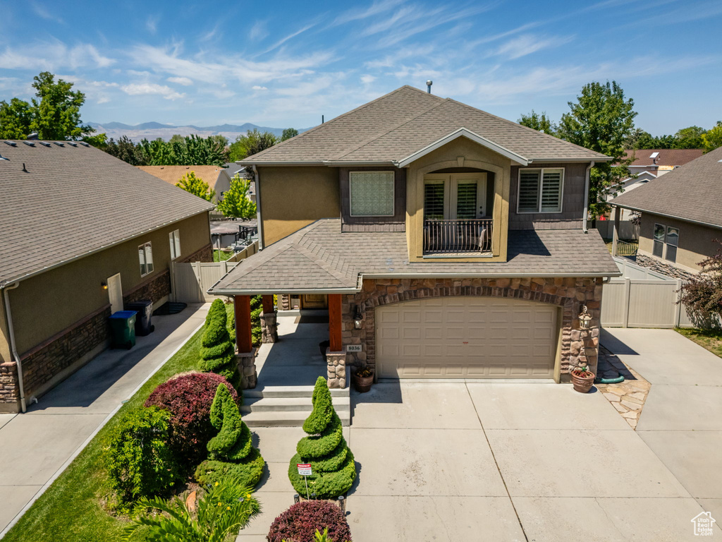 View of front facade featuring driveway, a garage, a shingled roof, and stone siding