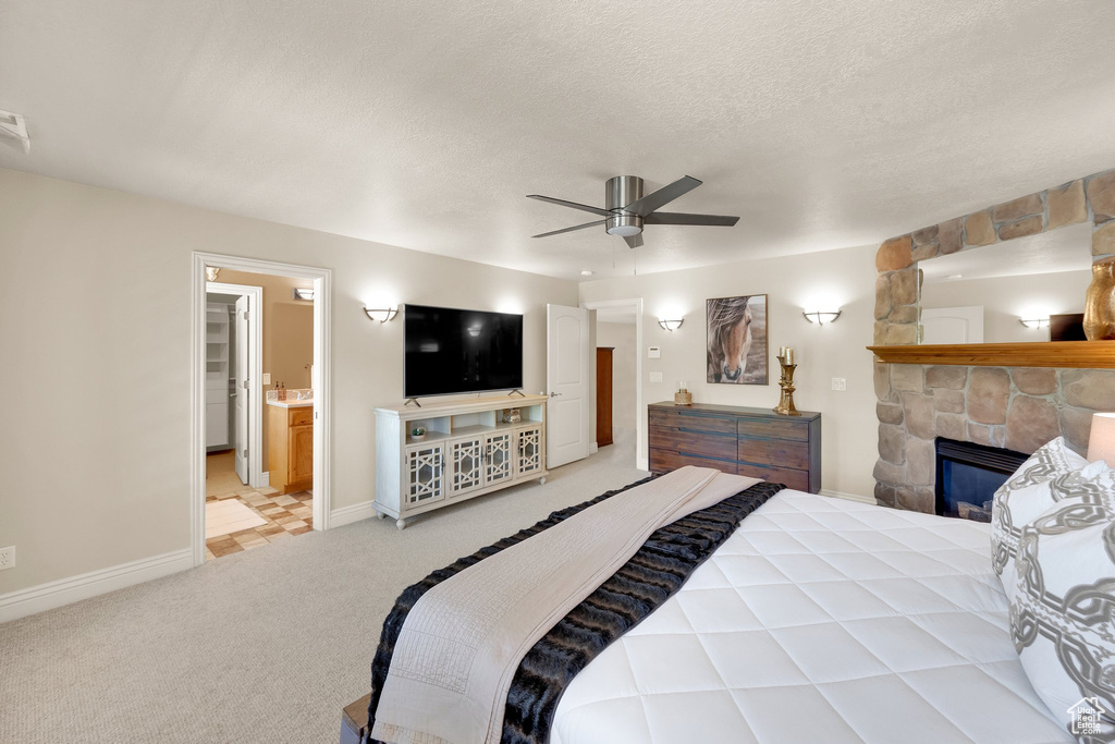 Bedroom with light colored carpet, baseboards, a stone fireplace, ceiling fan, and a textured ceiling