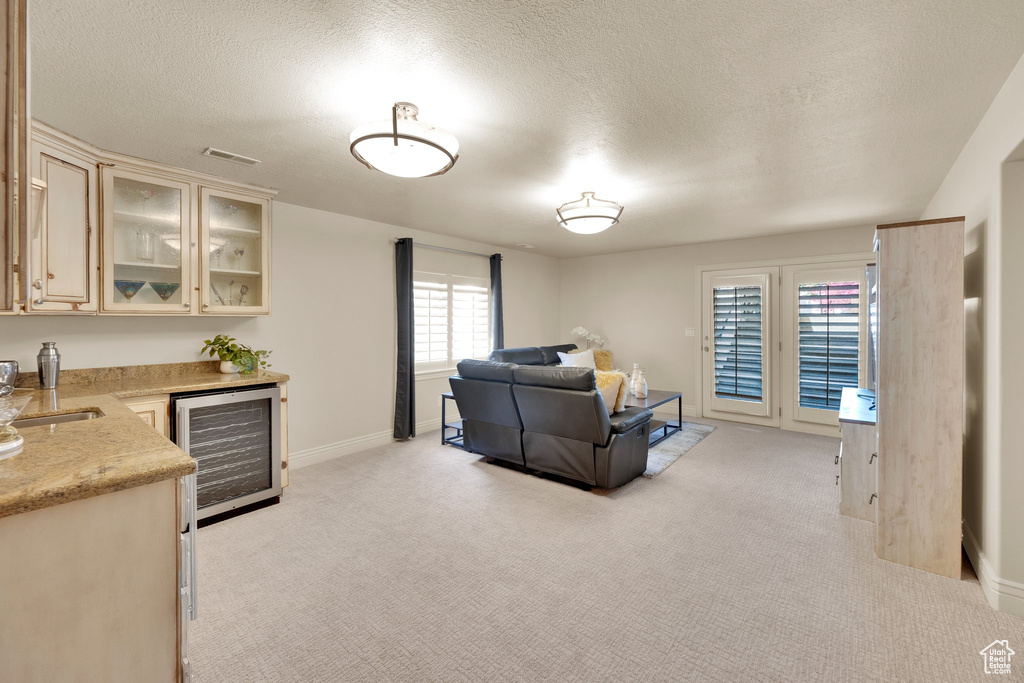 Living room with beverage cooler, bar area, light colored carpet, a textured ceiling, and baseboards