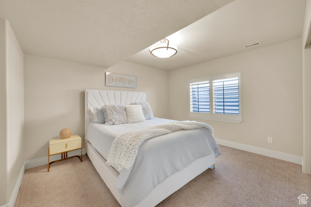 Bedroom featuring light carpet, baseboards, and a textured ceiling