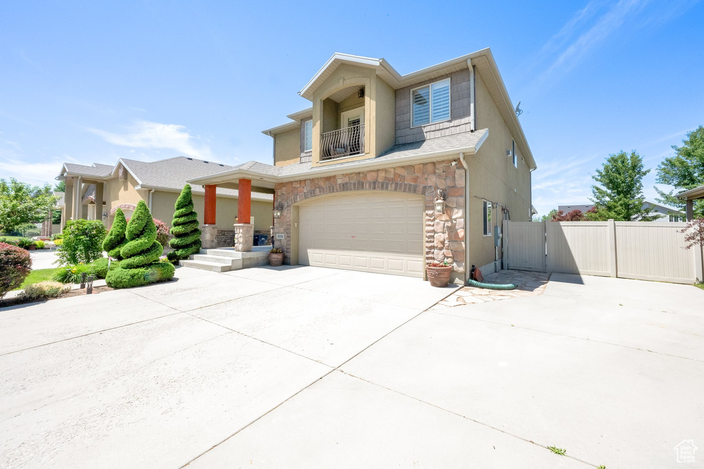 View of front of home featuring a balcony, an attached garage, driveway, stone siding, and a gate