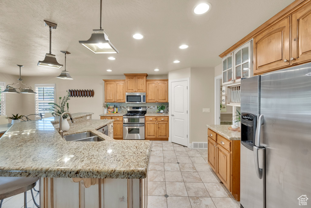 Kitchen featuring stainless steel appliances, a sink, recessed lighting, glass insert cabinets, and light stone counters