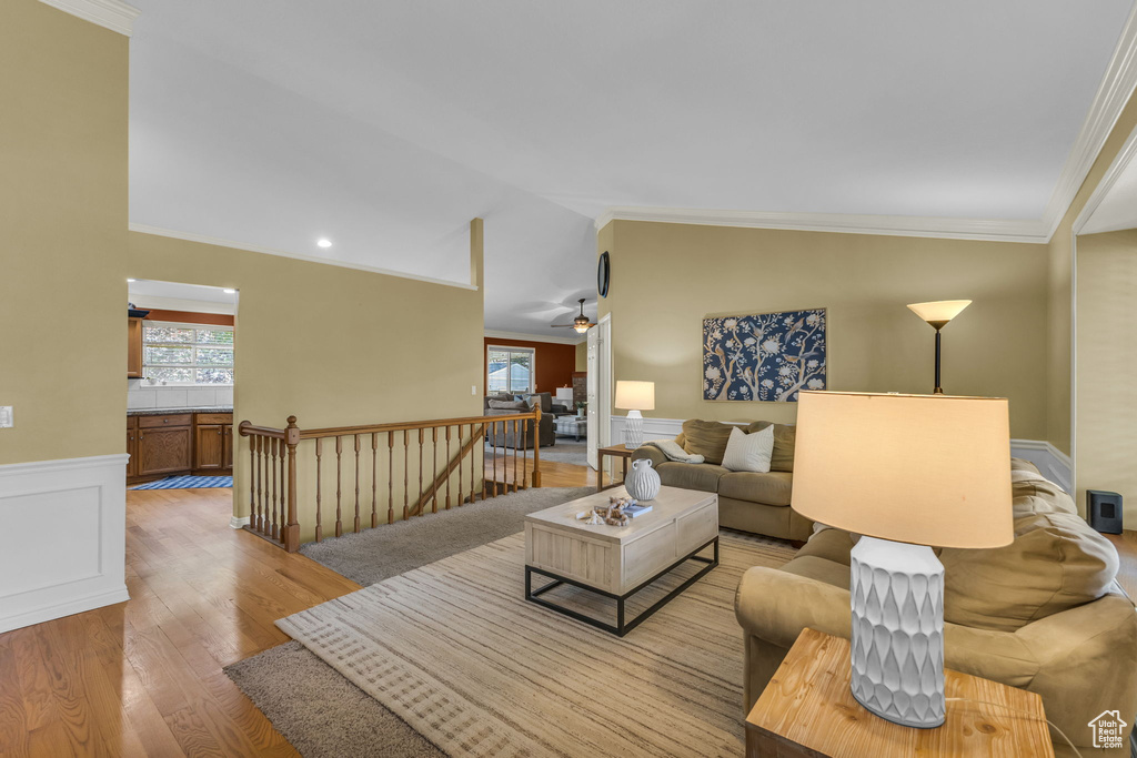 Living area with light wood-style floors, plenty of natural light, wainscoting, ornamental molding, and vaulted ceiling
