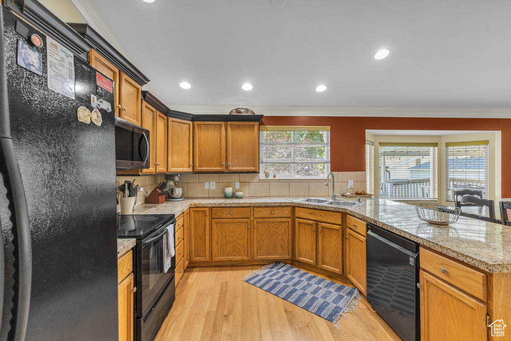 Kitchen featuring black appliances, a sink, crown molding, a peninsula, and light wood finished floors