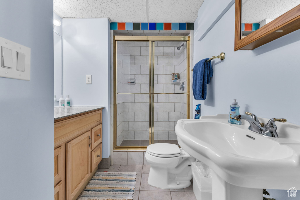 Bathroom featuring a shower stall, toilet, tile patterned floors, a textured ceiling, and a sink