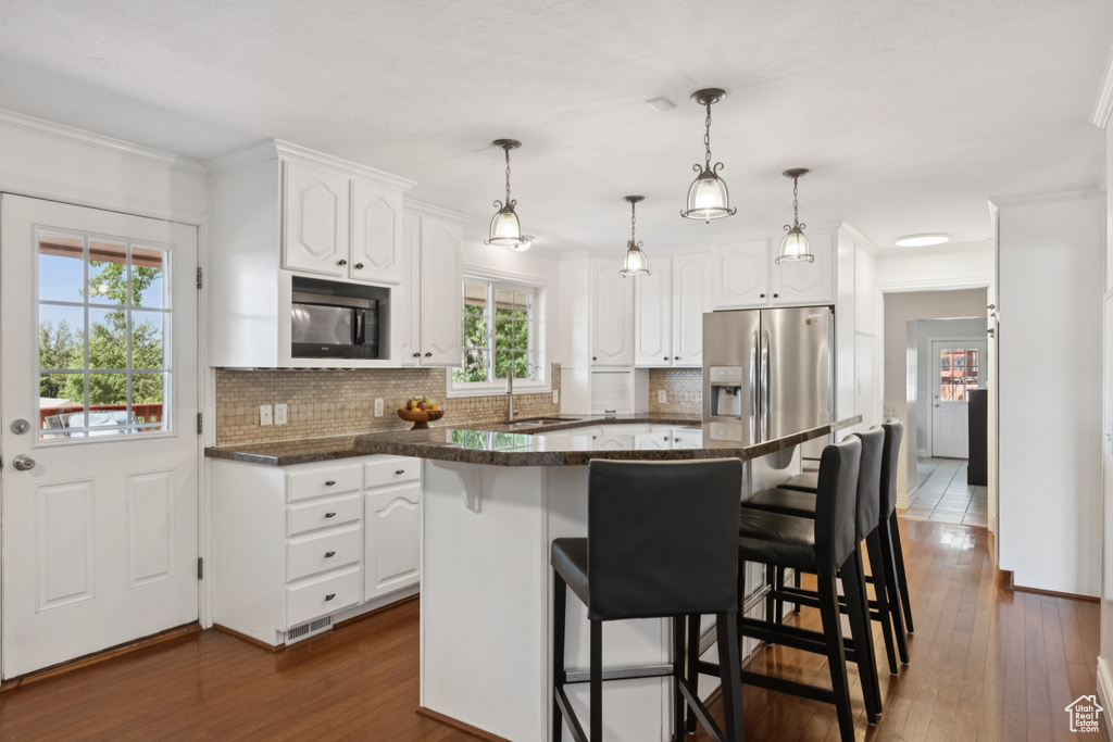 Kitchen with black microwave, white cabinets, stainless steel refrigerator with ice dispenser, a breakfast bar area, and decorative backsplash