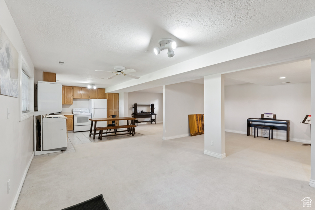 Kitchen featuring white appliances, a textured ceiling, light colored carpet, open floor plan, and ceiling fan