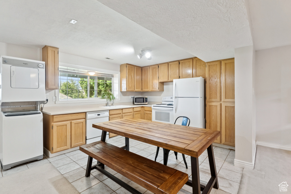Kitchen with white appliances, estacked washer and dryer, light countertops, light brown cabinetry, and a textured ceiling