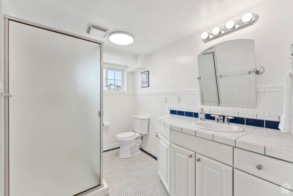 Full bathroom with vanity, a wainscoted wall, a shower stall, and tile patterned flooring