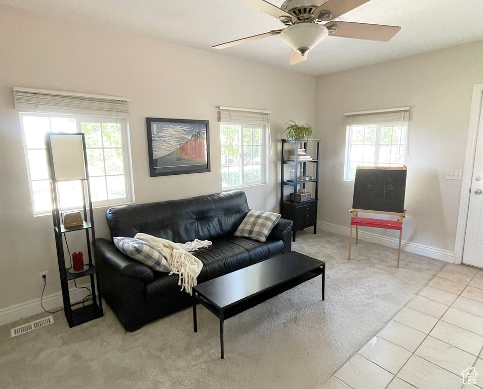 Living area featuring healthy amount of natural light, light colored carpet, a ceiling fan, and baseboards