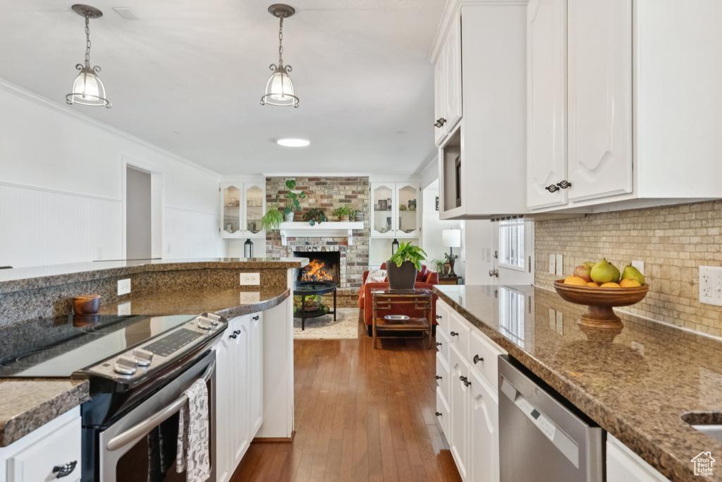 Kitchen with stainless steel appliances, a brick fireplace, white cabinets, and crown molding