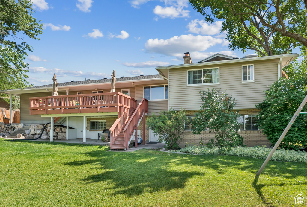 Back of house featuring stairway, a chimney, a deck, brick siding, and a yard
