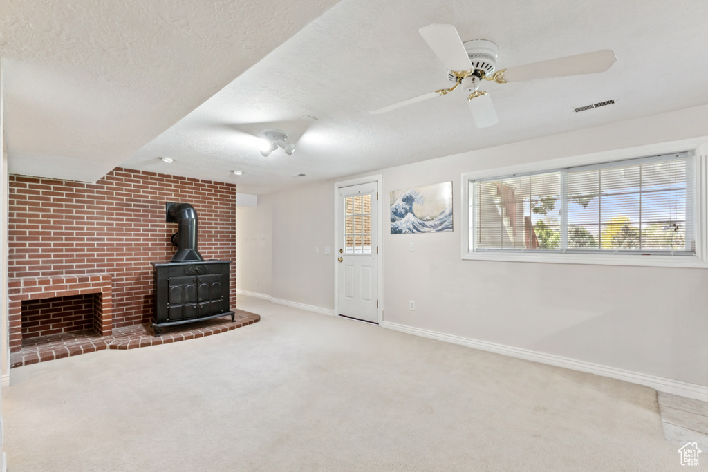 Unfurnished living room with carpet, a wood stove, a textured ceiling, and a ceiling fan
