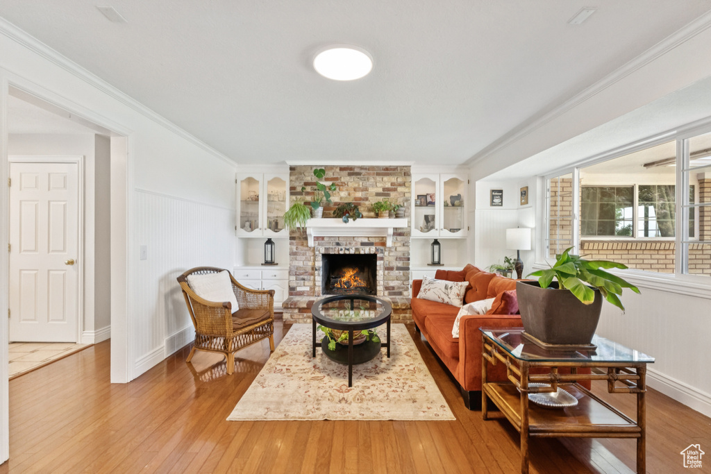 Living area featuring hardwood / wood-style floors, a brick fireplace, crown molding, and built in shelves