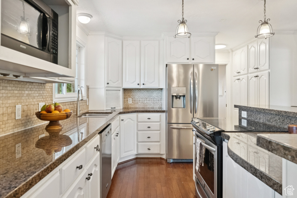Kitchen featuring stainless steel appliances, backsplash, white cabinetry, and dark stone counters