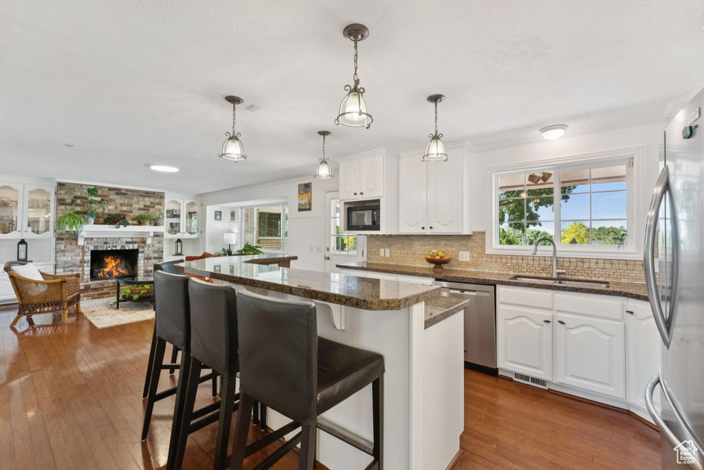 Kitchen with appliances with stainless steel finishes, dark wood finished floors, a kitchen breakfast bar, white cabinetry, and a large fireplace