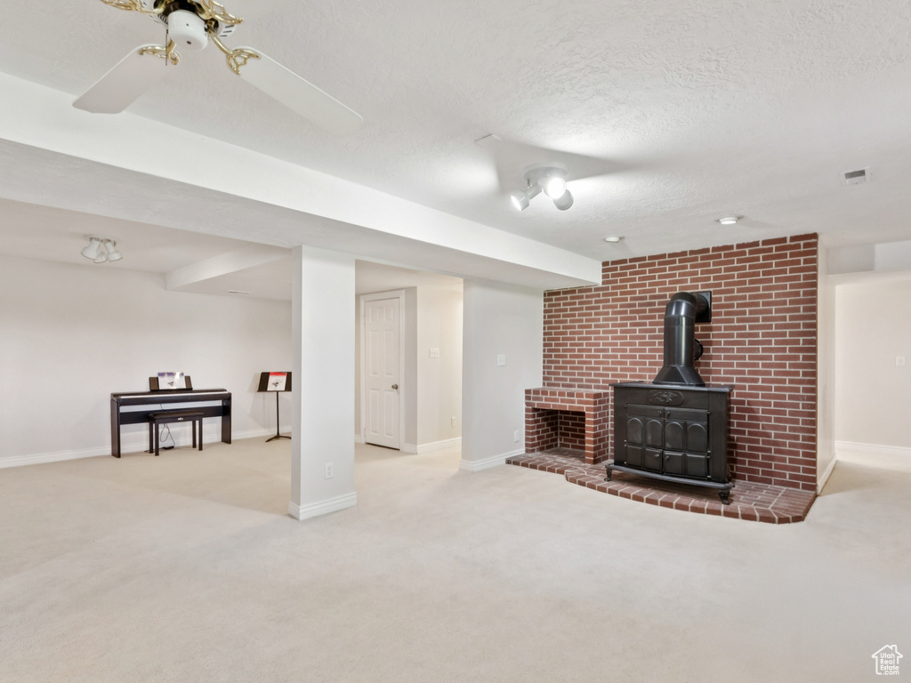 Unfurnished living room featuring carpet floors, a wood stove, a textured ceiling, and ceiling fan
