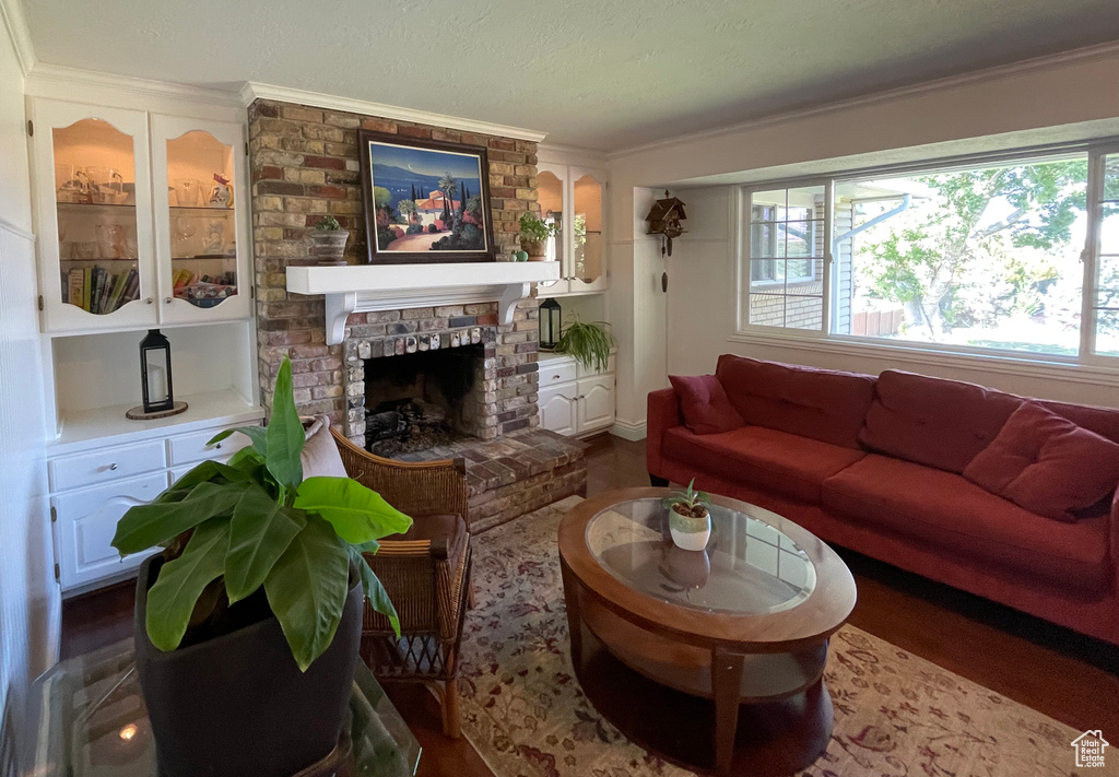 Living room with crown molding, a brick fireplace, and dark wood finished floors
