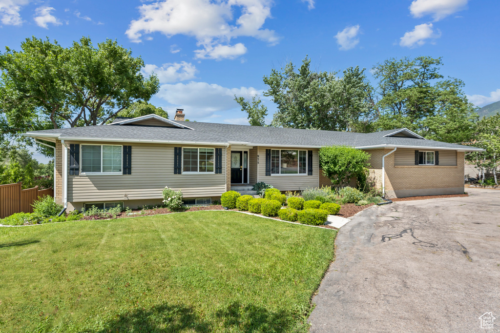 Ranch-style house featuring brick siding, a front lawn, driveway, a chimney, and roof with shingles