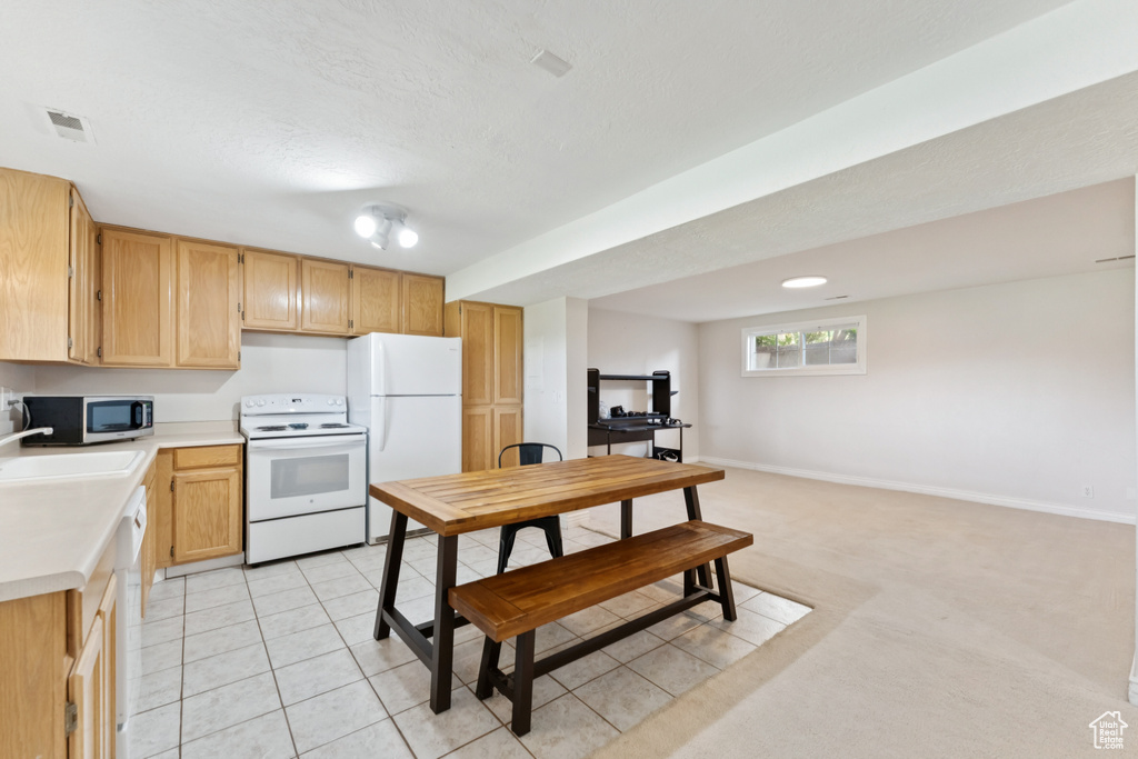Kitchen featuring white appliances, light countertops, light carpet, light tile patterned floors, and light brown cabinets