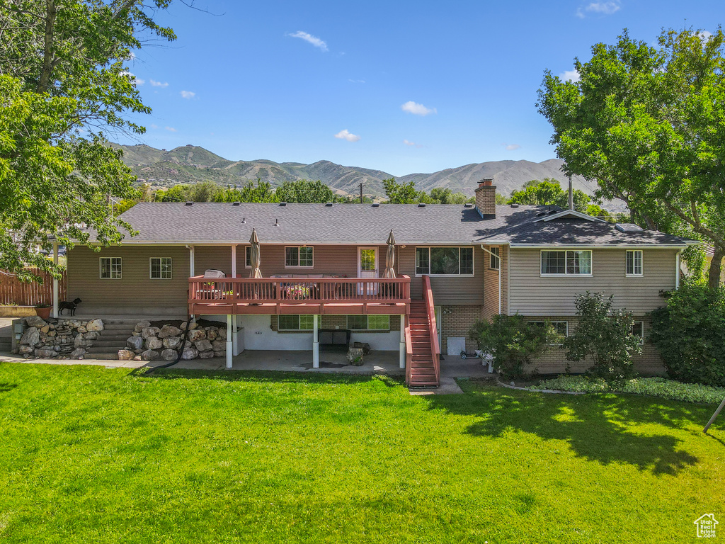 Back of property with a deck with mountain view, a patio area, stairway, a chimney, and a yard