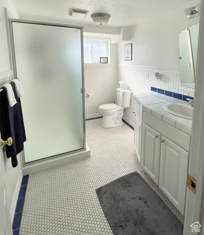 Full bath featuring vanity, a shower stall, wainscoting, and toilet
