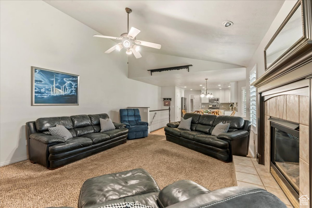 Living area featuring a tile fireplace, a ceiling fan, a chandelier, high vaulted ceiling, and light colored carpet