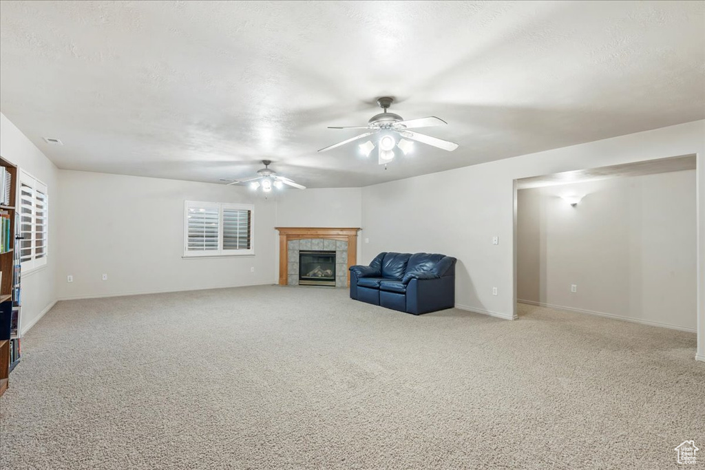 Unfurnished room featuring a tile fireplace, a ceiling fan, carpet floors, and baseboards