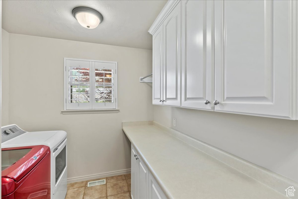 Laundry room featuring washing machine and dryer, cabinet space, baseboards, and light tile patterned floors