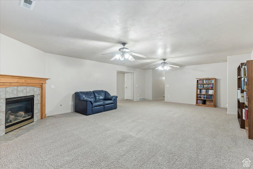 Unfurnished room with a tiled fireplace, a ceiling fan, carpet, and baseboards