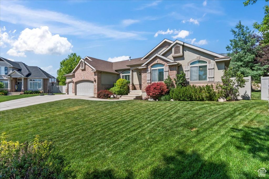 View of front facade featuring driveway, brick siding, a front yard, and an attached garage