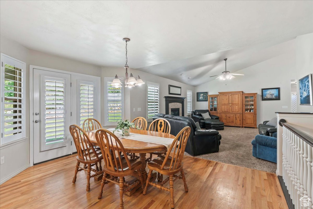Dining area featuring light wood-style floors, a fireplace, a chandelier, ceiling fan, and lofted ceiling
