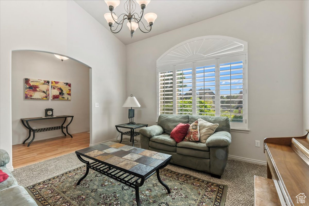 Living area with a chandelier, vaulted ceiling, arched walkways, baseboards, and wood finished floors
