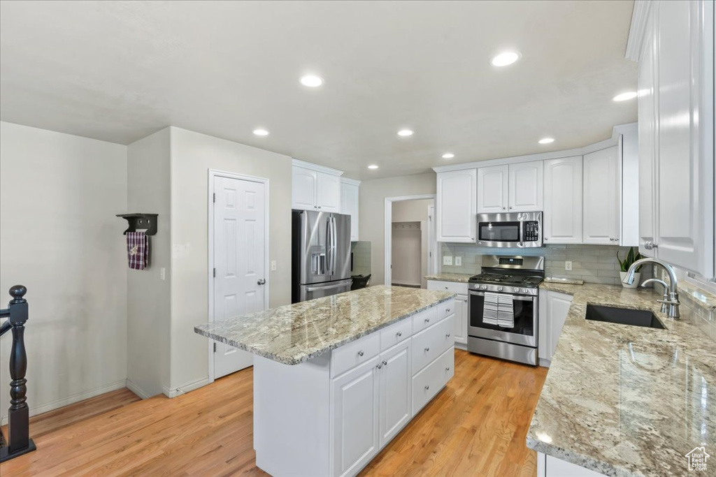 Kitchen with appliances with stainless steel finishes, a sink, a center island, light wood-style floors, and white cabinetry