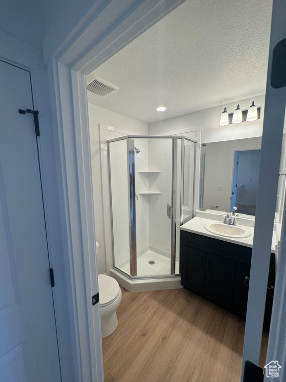Full bath with wood finished floors, toilet, vanity, a shower stall, and a textured ceiling