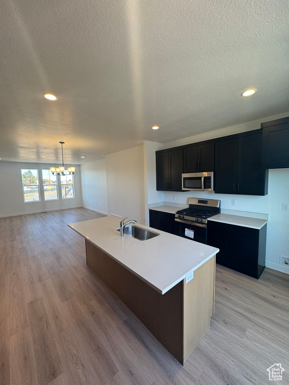 Kitchen with appliances with stainless steel finishes, a sink, dark cabinetry, a chandelier, and a textured ceiling