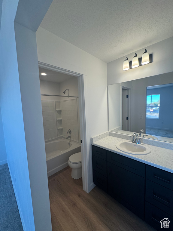 Bathroom with wood finished floors, vanity, toilet, bathing tub / shower combination, and a textured ceiling