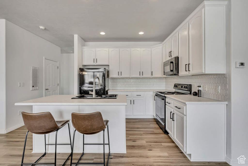 Kitchen featuring black electric range oven, freestanding refrigerator, a breakfast bar area, light wood-type flooring, and a kitchen island with sink