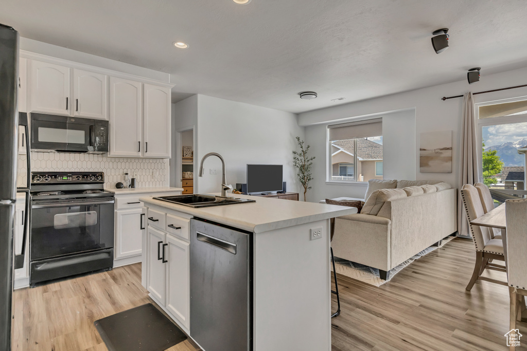 Kitchen with black appliances, a sink, open floor plan, light wood-style floors, and recessed lighting