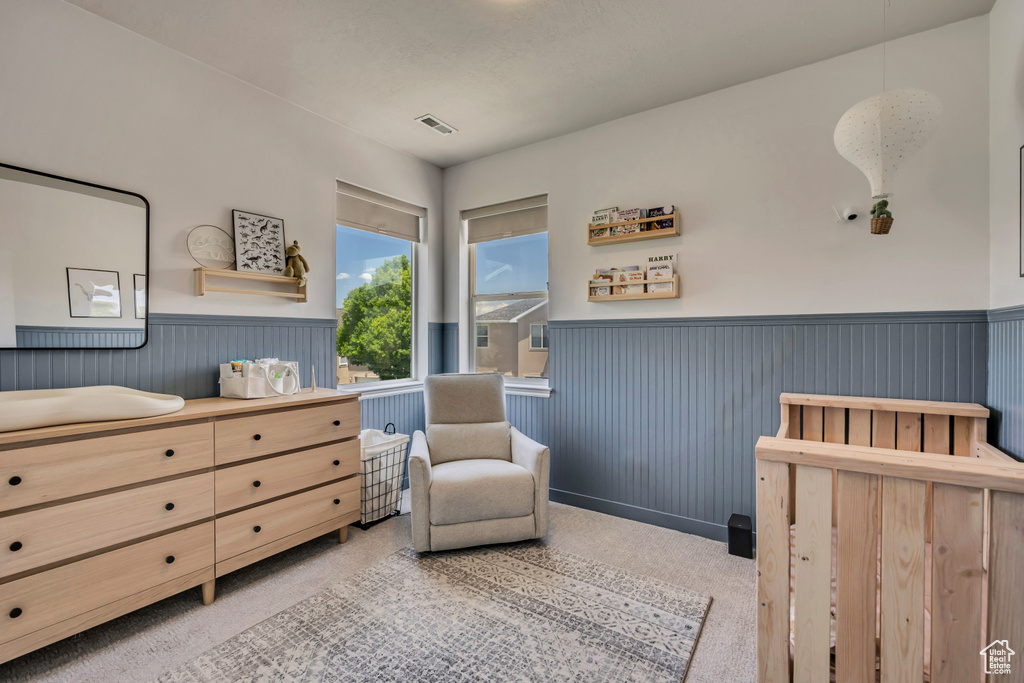 Bedroom featuring a wainscoted wall, a nursery area, and carpet flooring
