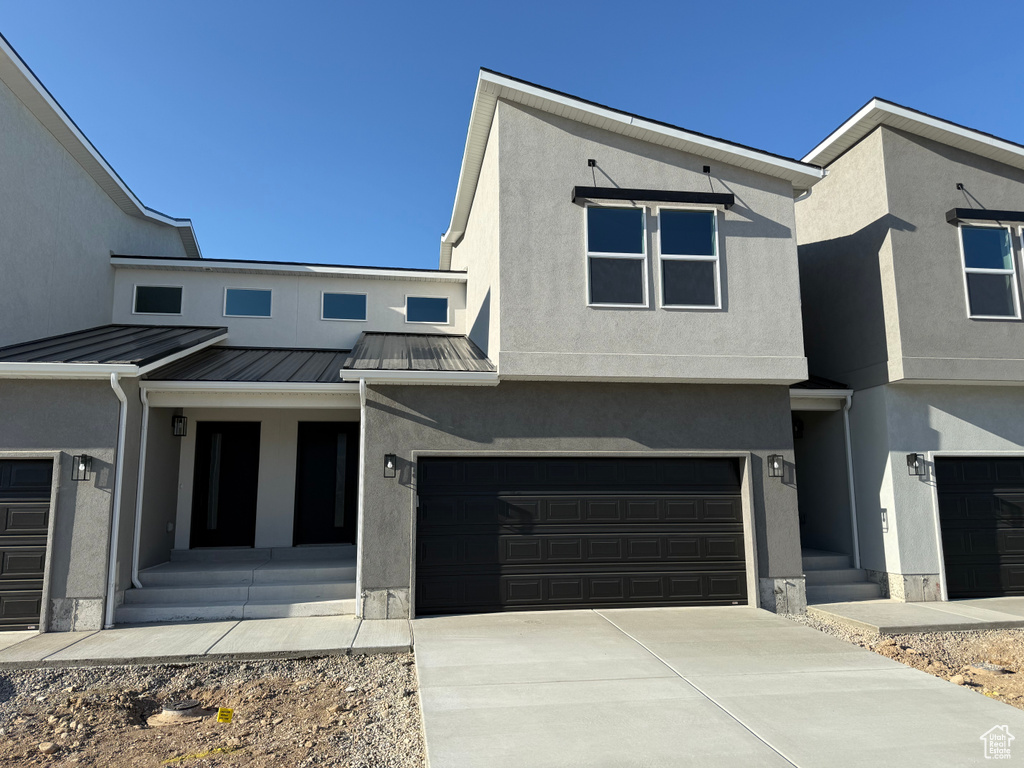 Townhome / multi-family property featuring a standing seam roof, stucco siding, a porch, driveway, and an attached garage